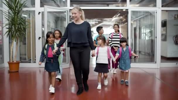 Colegiales multiétnicos caminando en el pasillo con tutor femenino. — Vídeo de stock