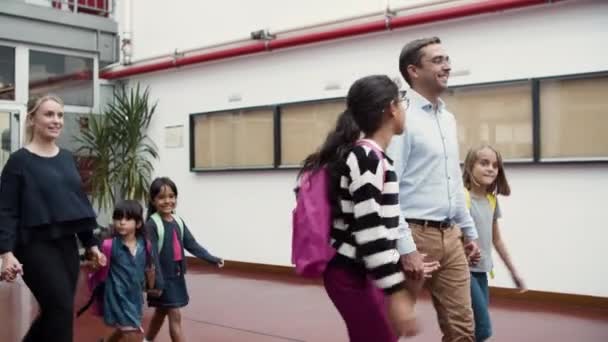 Άνδρες και γυναίκες δάσκαλοι περπατούν με παιδιά στο διάδρομο του σχολείου. — Αρχείο Βίντεο