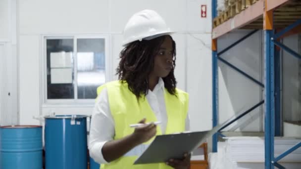 Serious female employee in helmet counting goods in stock. — Αρχείο Βίντεο