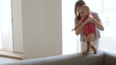 Annesinin yardımıyla kanepede yürüyen gülümseyen küçük kız.. 