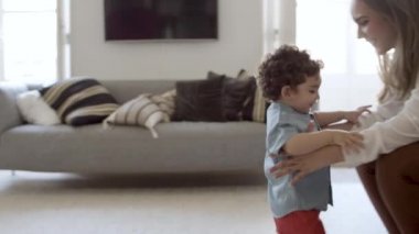 Odaklanmış çocuk ilk adımı atıyor, annesine doğru yürüyor..