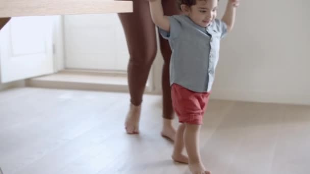 Счастливый мальчик делает первые шаги с помощью мамы дома. — стоковое видео