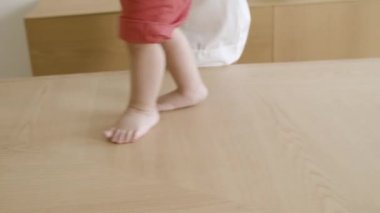 Annenin yardımıyla masanın üzerinde yürüyen erkek bebek bacaklarının yakın çekimi..