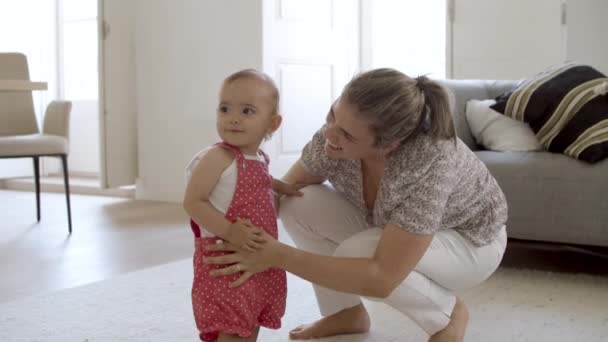 Glimlachend kind staat met hulp van moeder in de woonkamer. — Stockvideo