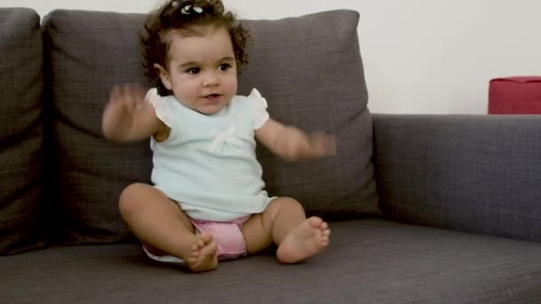 Kanepede oturmuş dans etmeye çalışan sevimli, neşeli bir bebek.. — Stok video