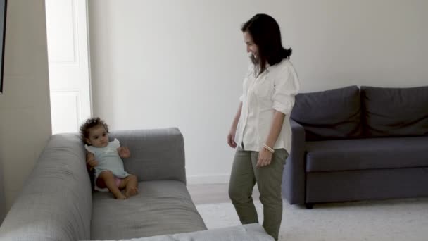 Alegre madre de pie junto a su hija sentada en el sofá. — Vídeos de Stock