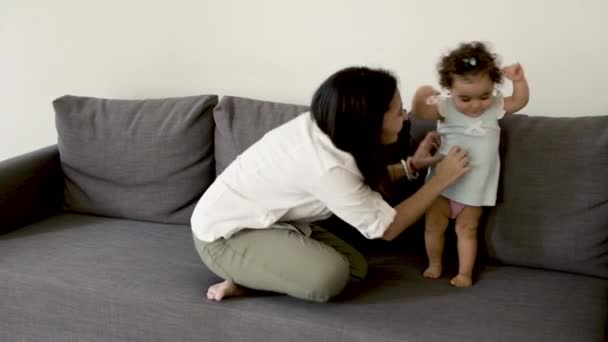 Feliz madre sentada en el sofá con su lindo bebé y divertirse. — Vídeos de Stock