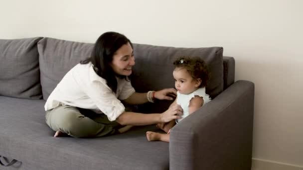 Счастливая мама, сидящая на диване, пытаясь заставить серьезного ребенка смеяться. — стоковое видео