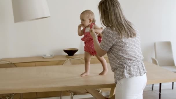 Opgewonden kind het nemen van haar eerste stappen op tafel, het houden van moeders hand. — Stockvideo