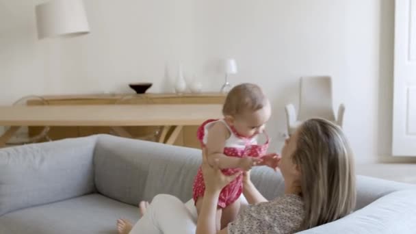 白人の母親はソファに寝そべって娘を頭上に持ち上げ. — ストック動画