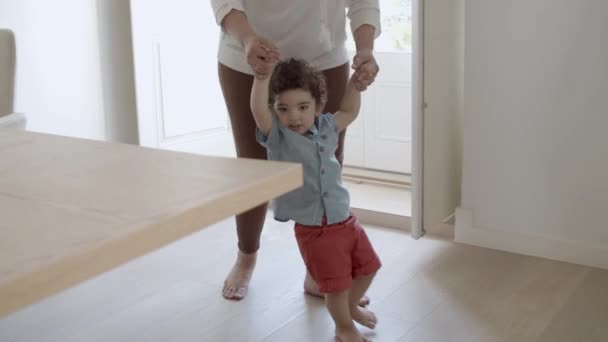 Bebê alegre tentando dar os primeiros passos sem a ajuda das mães. — Vídeo de Stock
