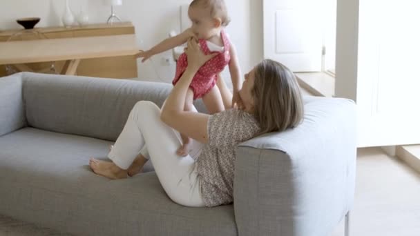 Caucasiana mãe deitada no sofá, levantando sua filha cansada. — Vídeo de Stock