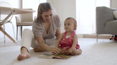 Neşeli anne ve kız yerde oturmuş kitap okuyorlar.. 