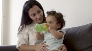Anneler dizlerinin üzerinde oturan, şişeden su içen tatlı bir bebek..