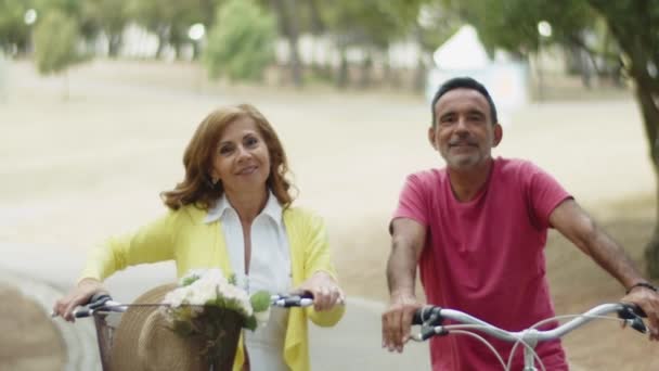 Bisiklette oturan ve kameraya el sallayan mutlu yaşlı çift. — Stok video