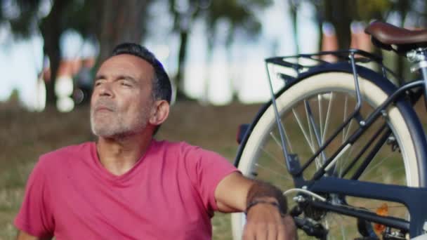 Senior siedzi na trawniku obok roweru w letnim parku — Wideo stockowe