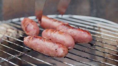 Izgarada sosis çeviren tanınmayan birinin yakın çekimi.
