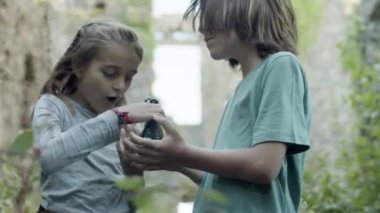 Gülen kız, hayrete düşmüş çocuğa cam taşlar veriyor. Eski şatonun arka planında durup eğlenen ve sihirbazcılık oynayan erkek ve kadın gençlerin yavaş çekimleri. Büyücülük, terk edilmiş bina konsepti.