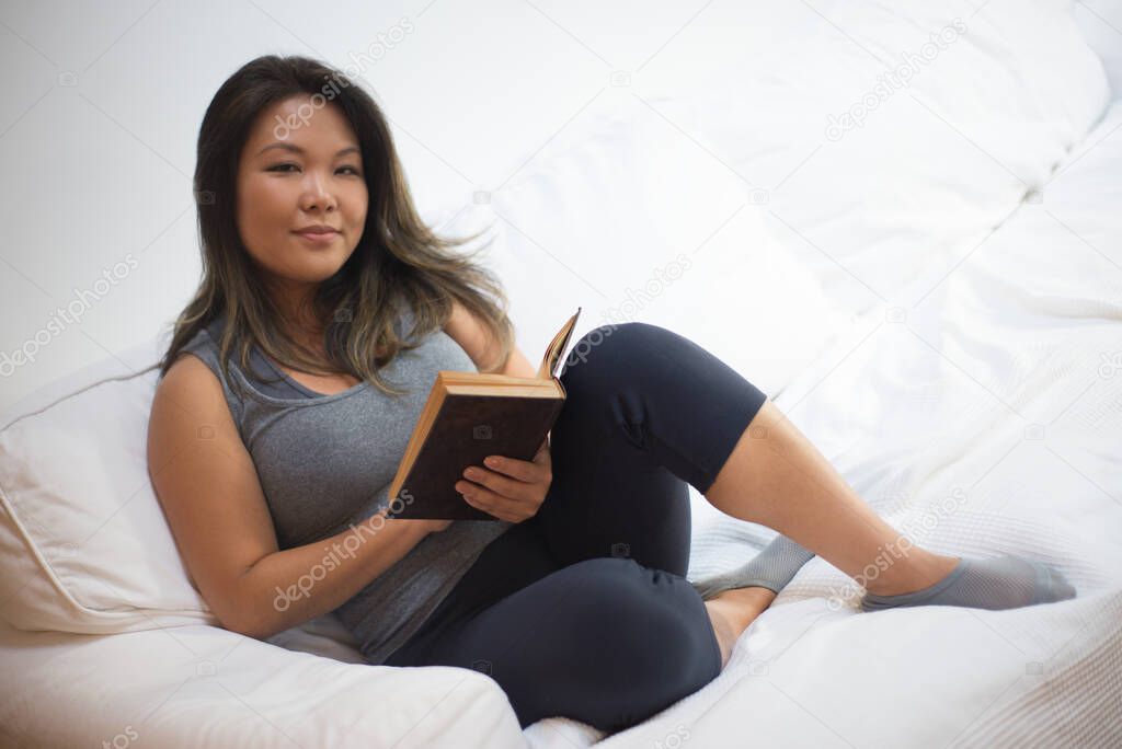 Calm beautiful Japanese woman reading book in bed