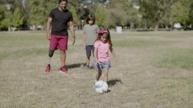 Engelli baba, oğul ve kızın top oynamaları ön planda.