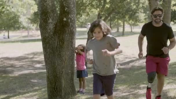 Fogyatékos apa bújócskázik a gyerekekkel a parkban. — Stock videók