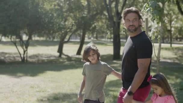 Vue latérale de l'homme handicapé se promenant avec des enfants dans le parc — Video