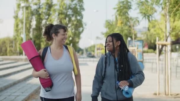 Spor giyim sektöründe mutlu bir kadın arkadaşıyla kol kola yürüyor. — Stok video