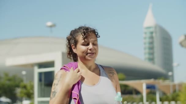 Mujer feliz caminando y bebiendo agua después de correr por la mañana — Vídeos de Stock