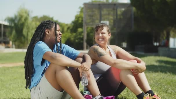 Vista laterale di amici sorridenti che riposano sul prato dopo l'allenamento — Video Stock