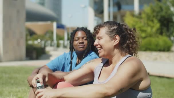 Вид збоку задоволених жінок закінчив тренування, сидячи на газоні — стокове відео