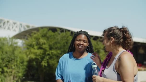 Kamerafahrt lächelnder Frauen, die nach dem Laufen Wasser trinken — Stockvideo