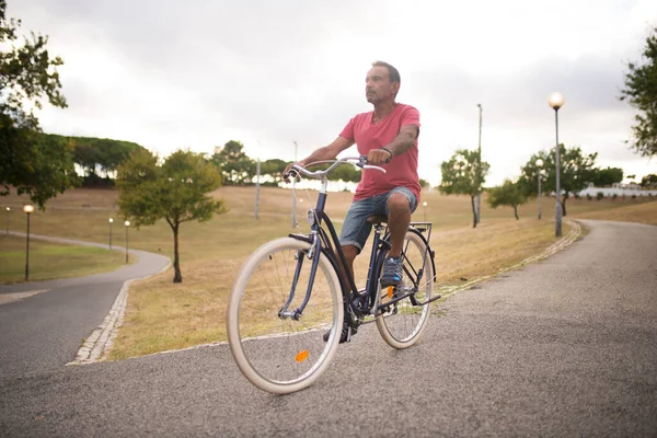 Homme mature confiant à vélo le long de la route du parc — Photo