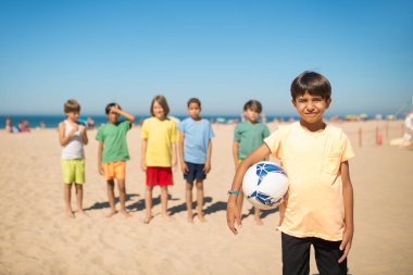 Kumsalda topla duran gülümseyen Arap çocuk.