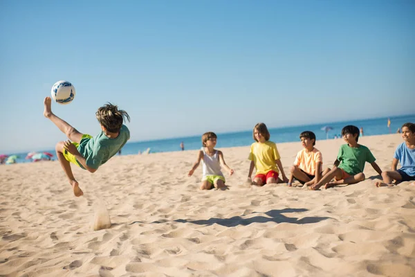 Genç bir çocuk plajda top sektiriyor.