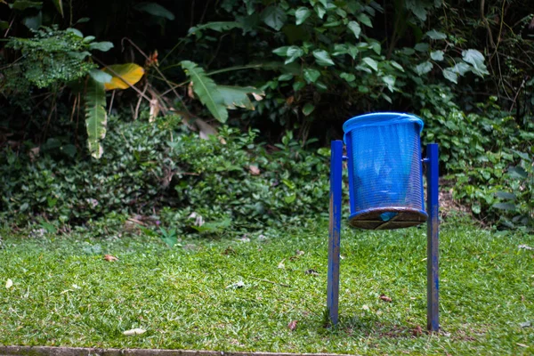 blue trash can in the middle of the green forest with a blue bag