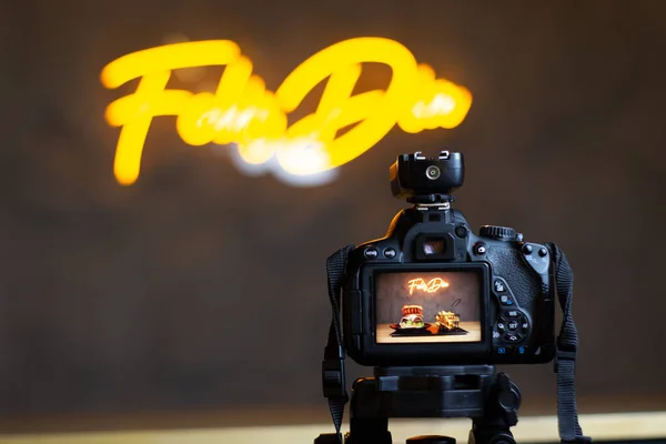 professional camera in front of a yellow neon sign with a fresh burger in front
