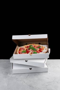 Et pizzası kutunun içinde. Beton masa ve siyah arka planda duran pizza kutuları..