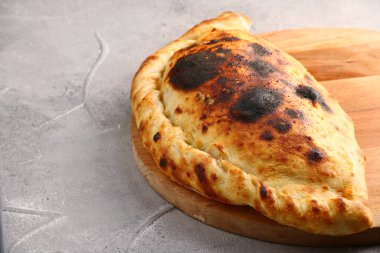 Pizza calzone, ahşap tahtaya yakın çekim. Gri beton masada yarı pizzaya katlanmış. Pizza konsepti.