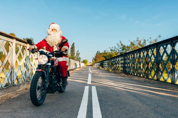 Noel Baba yolda motosiklet sürüyor.