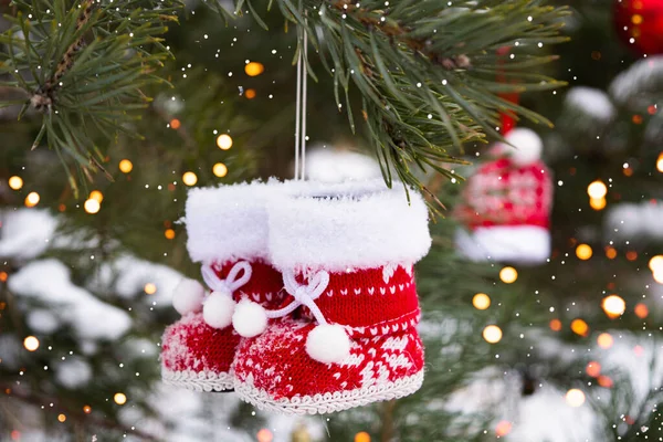Primer plano de pequeñas botas rojas de punto de Navidad colgando de un árbol en el bosque de invierno. —  Fotos de Stock