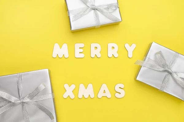 Caja de regalo, decoraciones grises sobre fondo amarillo y las palabras Feliz Navidad de letras de madera. —  Fotos de Stock