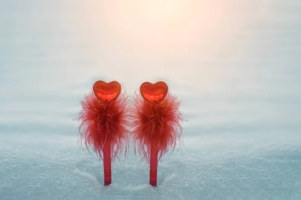 Coppia di penne rosse con decorazione a forma di cuore simboleggiano l'amore sullo sfondo della neve. San Valentino. — Foto Stock