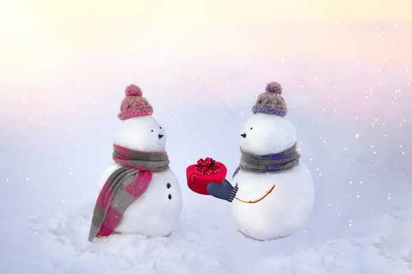 Muñecos de nieve enamorados con sombreros de invierno, bufandas sobre un fondo blanco en colores rosa y azul. Un chico dándole un regalo a su novia. Día de San Valentín, concepto de amor. 14 de febrero. — Foto de Stock
