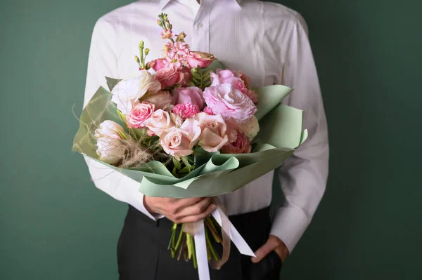 Man holding and giving a beautiful bouquet with flowers to woman on green background. Front view. Valentines, womens, mothers day, love concept.