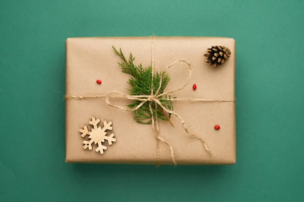 Kompozycja świąteczna z kraft pudełko z gałęzi iglastych, drewniane płatki śniegu na zielonym tle. — Zdjęcie stockowe