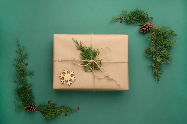 Composición navideña con caja regalo kraft con ramas de coníferas, copo de nieve de madera sobre fondo verde. —  Fotos de Stock