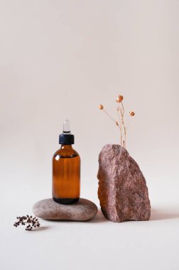 Taş podyumda cam bir şişede kozmetik, bej arka planda kurutulmuş çiçek. Ön görünüm.