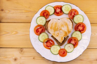 Beyaz tabakta salatalık ve domatesli kalp şeklinde tavuk dilimi. Yukarıdan bak. Ahşap arka. Boşluğu kopyala