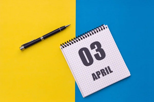 4月3日 3ヶ月の日 スパイラルとペンのあるノートブックは 黄色の青の背景 フラットレイアウト コピースペースにあります ロイヤリティフリーのストック写真