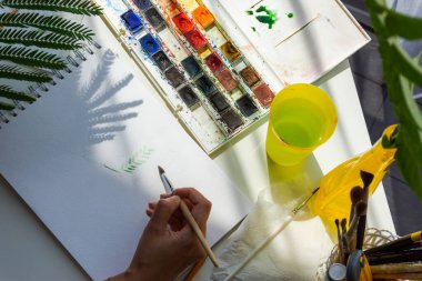 Suluboya çizimi en üstteki görünüm. Kız suluboya resimler çiziyor. Stüdyoda yaratıcı bir süreç. Sanatçının stüdyosu.